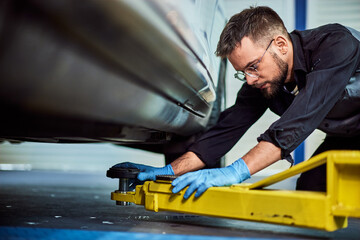 Photo of a mechanic lifting the car on the crane, checking a place to position the crane.