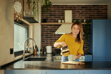 A portrait of a beautiful woman, pouring a coffee into the cup, in the kitchen.