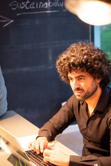 The image captures a north african man with curly hair deeply engrossed in his work on a laptop....