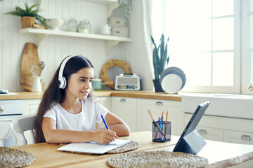 Preteen 12s girl in wireless headphones sit at table e-learning