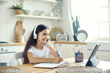 Preteen 12s girl in wireless headphones sit at table e-learning - obrazy, fototapety, plakaty