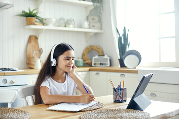 Preteen 12s girl in wireless headphones sit at table e-learning