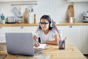 Girl in headphones and eyeglasses e-learning at home