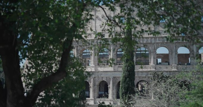 Amazing cinematic veiw of ancient Colosseum from amoung Parco Celio trees, establishment shot