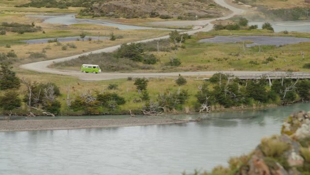 Panning shot of an old vw campervan driving down a dirtroad and over a bridge in torres del paine nationalpark in patagonia, chile