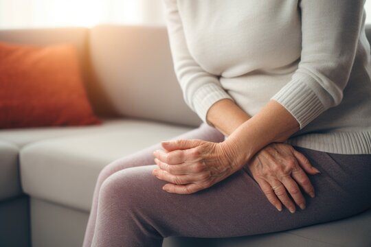 A woman is sitting on a couch, holding her hands. This image can be used to depict relaxation, meditation, or contemplation