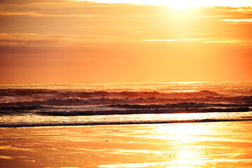 The beach is at low tide at dawn with a magnificent variety of colors in the sky. Tranquil sunrise view of the ocean coast.
