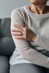 A woman sitting on a couch with her hands resting on her chest. This image can be used to depict relaxation, contemplation, or a moment of reflection