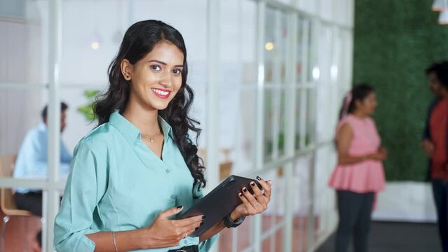 confident young woman employee standing at office by looking camera with tab in hand - concept of businesswoman, startup entrepreneur and career growth