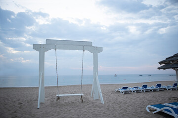 Wooden swing on the beach. The coast of the Indian Ocean. A deserted beach. The concept of summer holidays. Sun loungers on the beach.