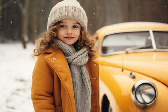 Little attractive girl dressed in winter jacket standing in front of retro car decorated for new year during snowfall