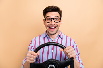 Photo of young astonished student young man holding steering wheel driving on road dangerous driver isolated over beige color background
