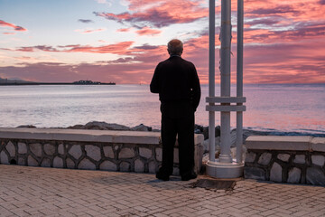 Paseo marítmo de Málaga, amanecer sobre el mar, hombre tercera edad visto de espaldas, mirando los primeros rayos de sol, vida saludable, tranquilidad, soledad