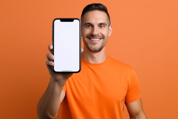 Fototapeta na wymiar Mobile App Advertisement. Handsome Excited Man Showing Pointing At White Empty Smartphone Screen Posing Over Orange Studio Background, Smiling To Camera. Check This Out, Cellphone Display Mock Up