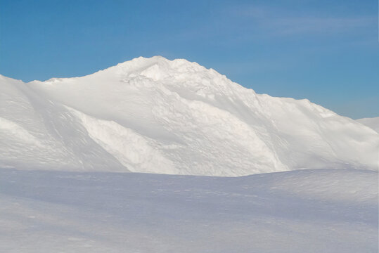 the image shows a majestic mountain range blanketed in pristine white snow. The peaks rise sharply into the sky, their jagged edges contrasting with the smooth, undulating slopes below. 