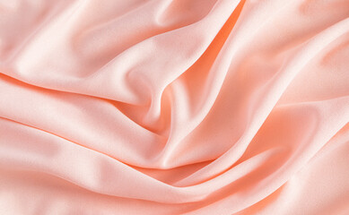 Elegant satin fabric with a peachy color. luxurious texture of the soft folds . festive background. design. color of the year peachy fuzz