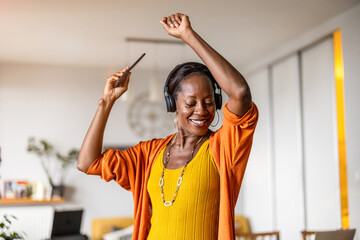 Woman listening to music with headphones connected to her smartphone in the living room at home
