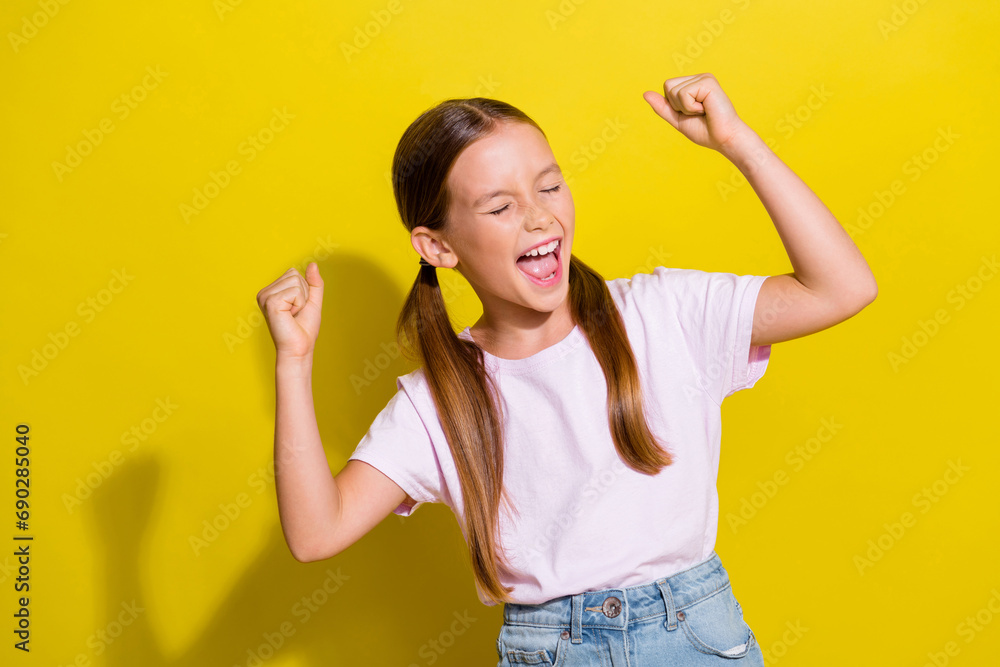 Poster Photo of sweet excited little child dressed pink t-shirt shouting yeah rising fists isolated yellow color background