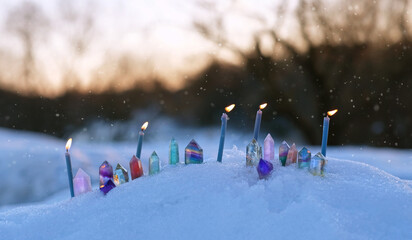 quartz minerals and burning candles in snow, winter nature background. Gemstones for esoteric...