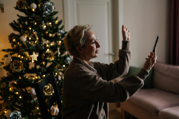 Side view of happy middle-aged woman holding smartphone make video call on Christmas Eve...