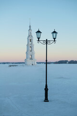 Fototapeta premium The city lantern against the background of an old bell tower on the frozen Uglich reservoir on January morning. Kalyazin. Tver regiont, Russia