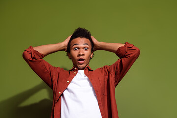Photo of speechless man with afro hair dressed brown shirt hold hands on head astonished staring isolated on khaki color background
