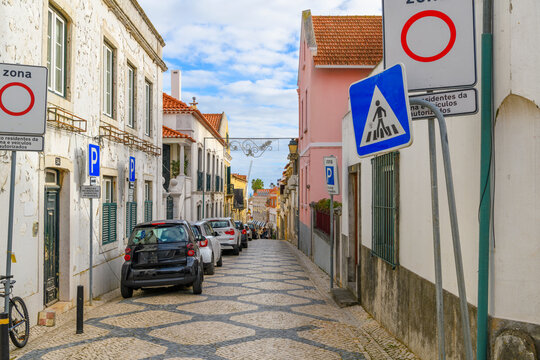 An empty narrow street of shops and cafes with the traditional cal&ccedil;ada pavement design in the old town of Cascais, Portugal.