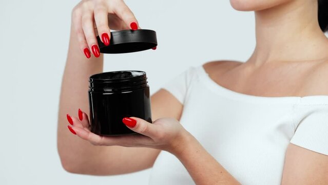 Hands of a young woman holding a container with body and skin care cream. Organic cosmetic product isolated on white background. Advertising and skin care concept.
