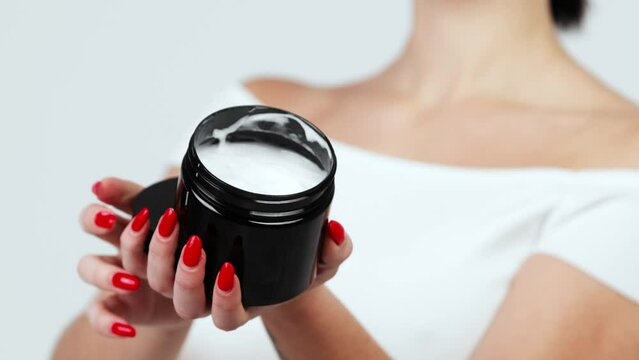 Hands of a young woman holding a container with body and skin care cream. Organic cosmetic product isolated on white background. Advertising and skin care concept.
