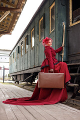 A beautiful girl in a burgundy suit of the last century and a hat with a veil stands with a...