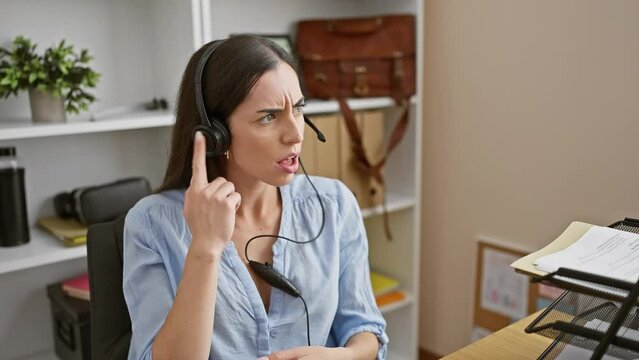 Clueless at the workplace, young beautiful hispanic woman wearing headset is all arms and no idea in office, her confused expression painting a portrait of bewildering emotions.