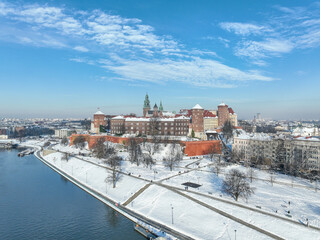 Krakow, Poland. Royal Wawel Cathedral and castle covered with snow in winter. Vistula river and tourist boats. Aerial view with boulevard, promenades and  walking people. Old city in the background
