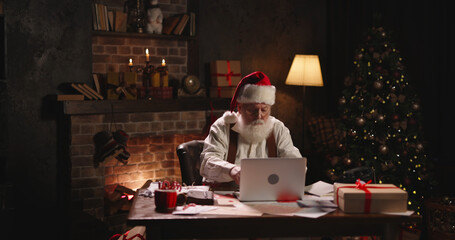 Bearded Santa Claus using laptop, outside view through window, typing on keyboard, buying New Year...