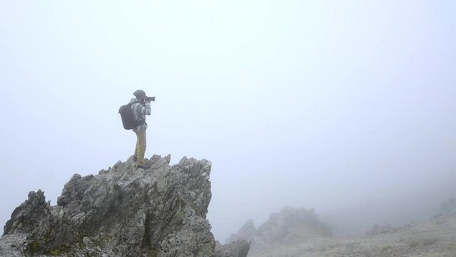 Slow motion video of a young man taking photos on a rock on an inactive volcano in Mexico with a lot of fog, called Nevado de Toluca.