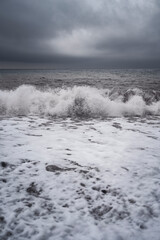 Landscape of stormy sea with rolling wave and foam on the beach with stormy gray sky, Crimea