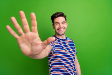 Photo of optimistic friendly handsome guy with stubble dressed striped t-shirt give you highfive isolated on green color background