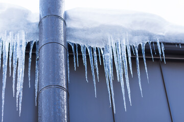 Frosted chimney pipe and icicles hanging from eaves of roof on cold day in snow background, winter thaw, spring concept