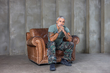 A soldier in camouflage, a soldier sitting in an armchair.A mature male bodybuilder in a military...