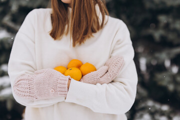 A beautiful girl in white knitted clothes holds mandarins in winter