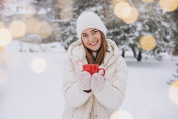 Cute happy woman holding hot coffee with candy canes in winter park