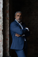 A handsome middle-aged man in a blue formal suit poses on a gray background. Portrait of a businessman. A handsome middle-aged man poses on a gray background with a place to copy