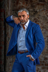 A handsome middle-aged man in a blue formal suit poses on a gray background. Portrait of a businessman. A handsome middle-aged man poses on a gray background with a place to copy