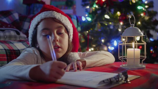 Cute little girl writes a letter to Santa Claus near the Christmas tree