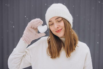 Happy woman in knitted mittens holding a snow heart on a winter snowy day