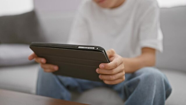 Adorable blond boy, comfortably sitting on sofa at home, using touchpad gadget, a glimpse of today's child's tech-driven lifestyle in a cosy living room