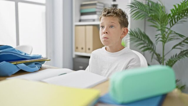 Adorable blond boy, an uncertain student, in a classroom setting, seated, clueless, studying books but seeming indifferent, embodies the classic 'i don't know' academic gesture.