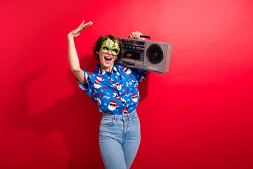 Portrait of overjoyed pretty lady carry boombox dance enjoy x-mas event empty space isolated on vivid red color background