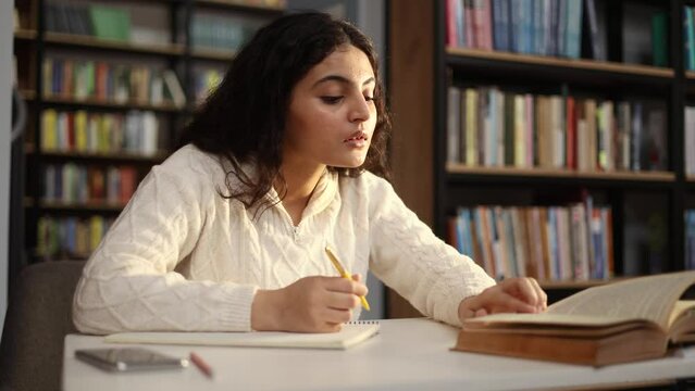 Pretty young woman student writes notes in textbook for essay study for class preparing for exams test make research for project using books literature at university library
