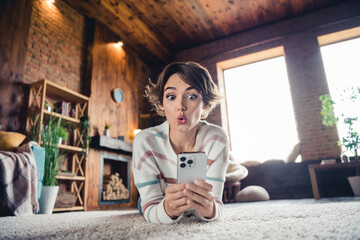 Full body portrait of impressed speechless lady lay floor use smart phone read unexpected news comment apartment inside