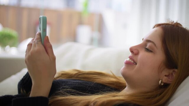 Happy young woman relax on comfortable couch using social media, searching information on browser wireless internet, online shopping, watching short videos.